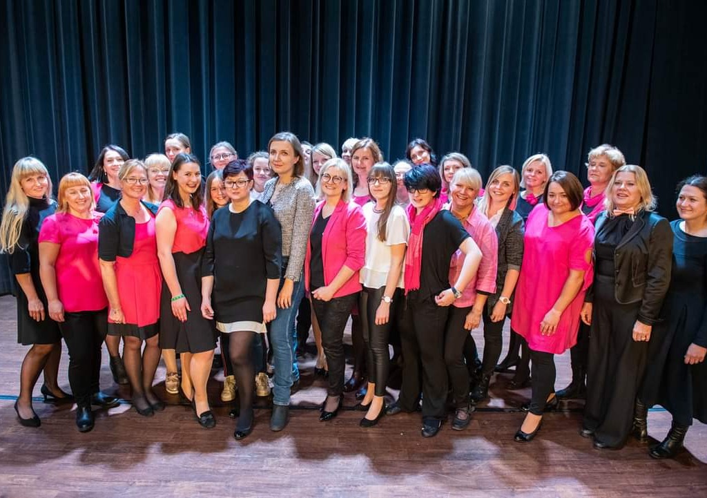 Grupa kobiet ubranych w czarne i różowe kolory stojąca na scenie