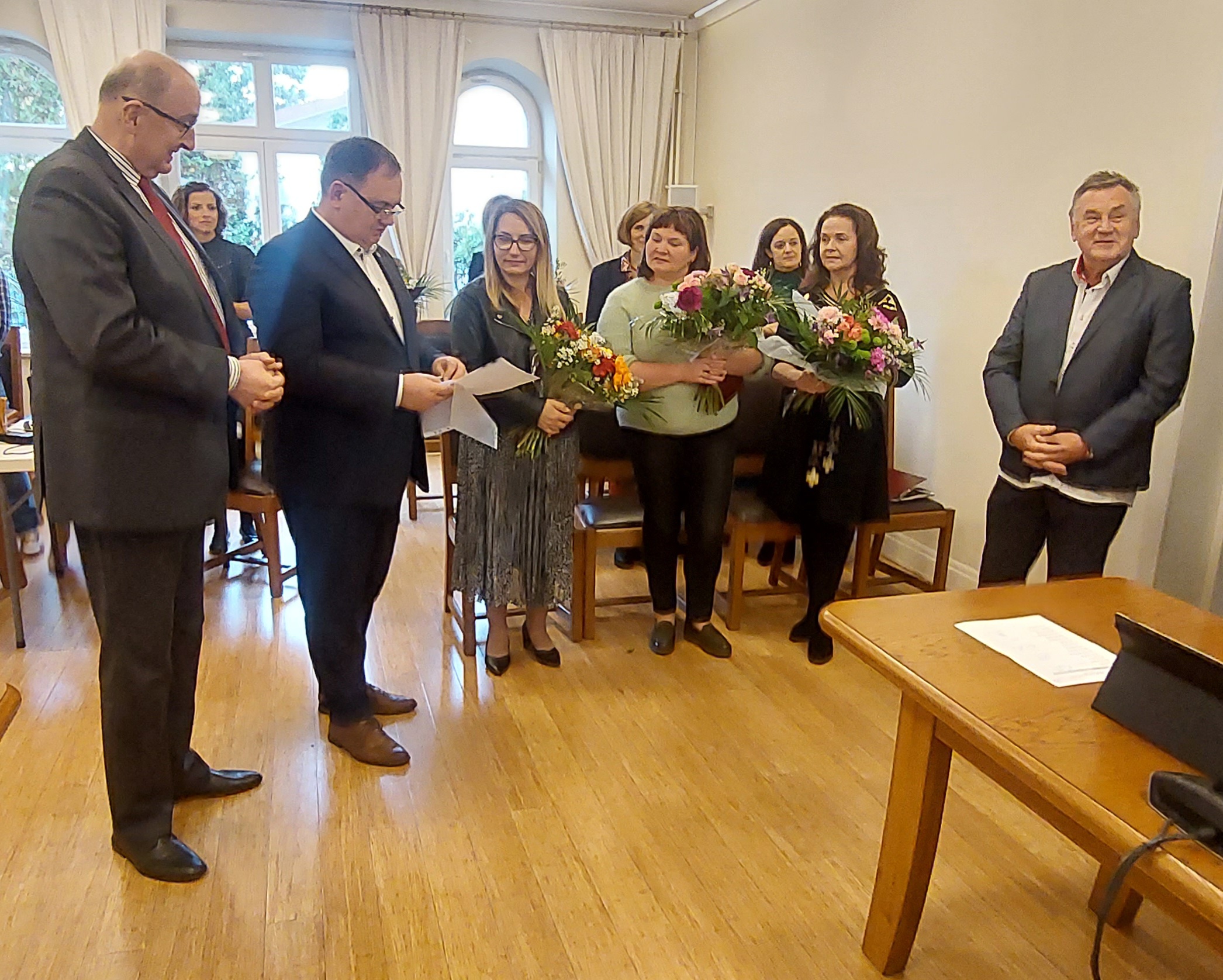 Po prawej stronie stoi Janusz Prządka, po lewej burmistrz Marek Banaszek i przewodniczący RM Mariusz Batorski. Między nimi stoją nauczycielki z kwiatami.