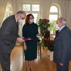 Burmistrz Marek Banaszek i kierownik USC Marzena Szczęśniak wręczają medal, kwiaty i dyplom małżonkowi