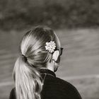 nastolatka z kucykiem stoi tyłem. Ma długie jasne włosy związane w kucyk, okulary i kwiat za uchem. Zdjęcie jest czarno-białe.