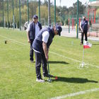 Dwóch mężczyzn w ciemnych spodniach, granatowych kamizelkach i białych koszulkach z herbem Ground Golf Józefów gra w ground golfa.