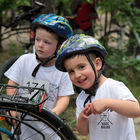 Dwoje małych dzieci w kaskach rowerowych przy rowerze