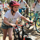 Dziewczynka prowadzi rower. W tle kilku innych rowerzystów.