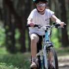 Dziecko w białej koszulce, kasku i okularach słonecznych jedzie na biało-niebieskim rowerze.